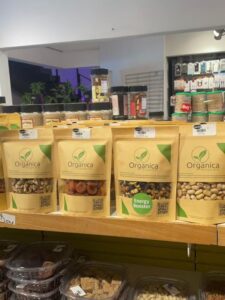 Shelf display of Organica premium dry fruits including organic walnuts, sun-dried apricots, Energy Booster mix, and pistachios in eco-friendly packaging.